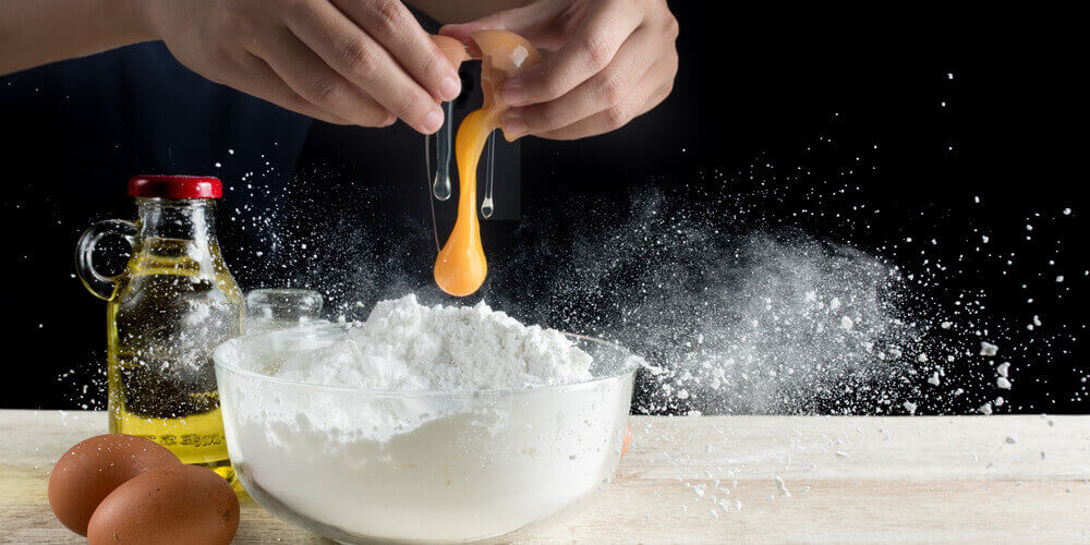 Hands cracking an egg into a bowl and flour flying everywhere 
